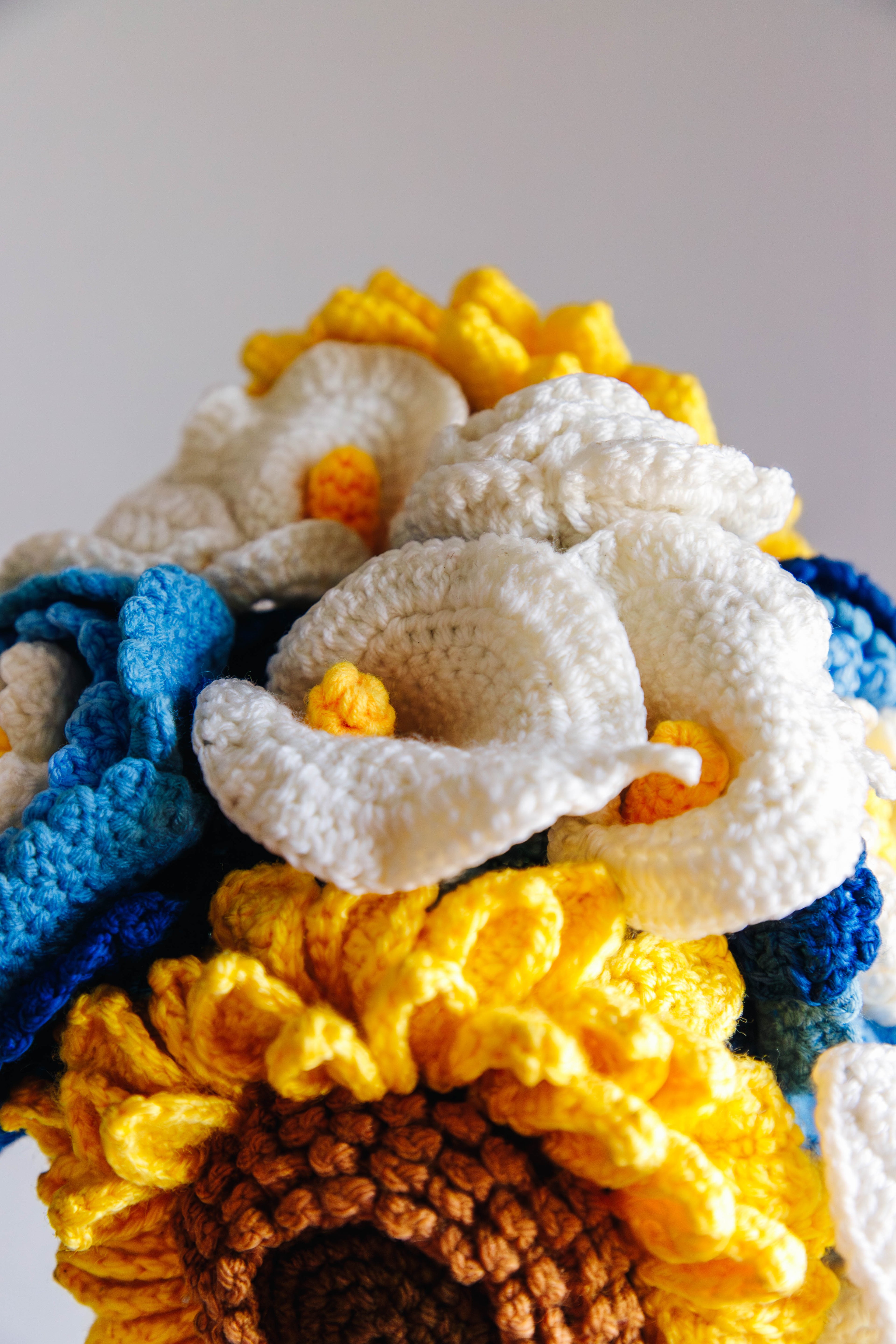 Close-up of crocheted flowers in blue, yellow, and white on a white background