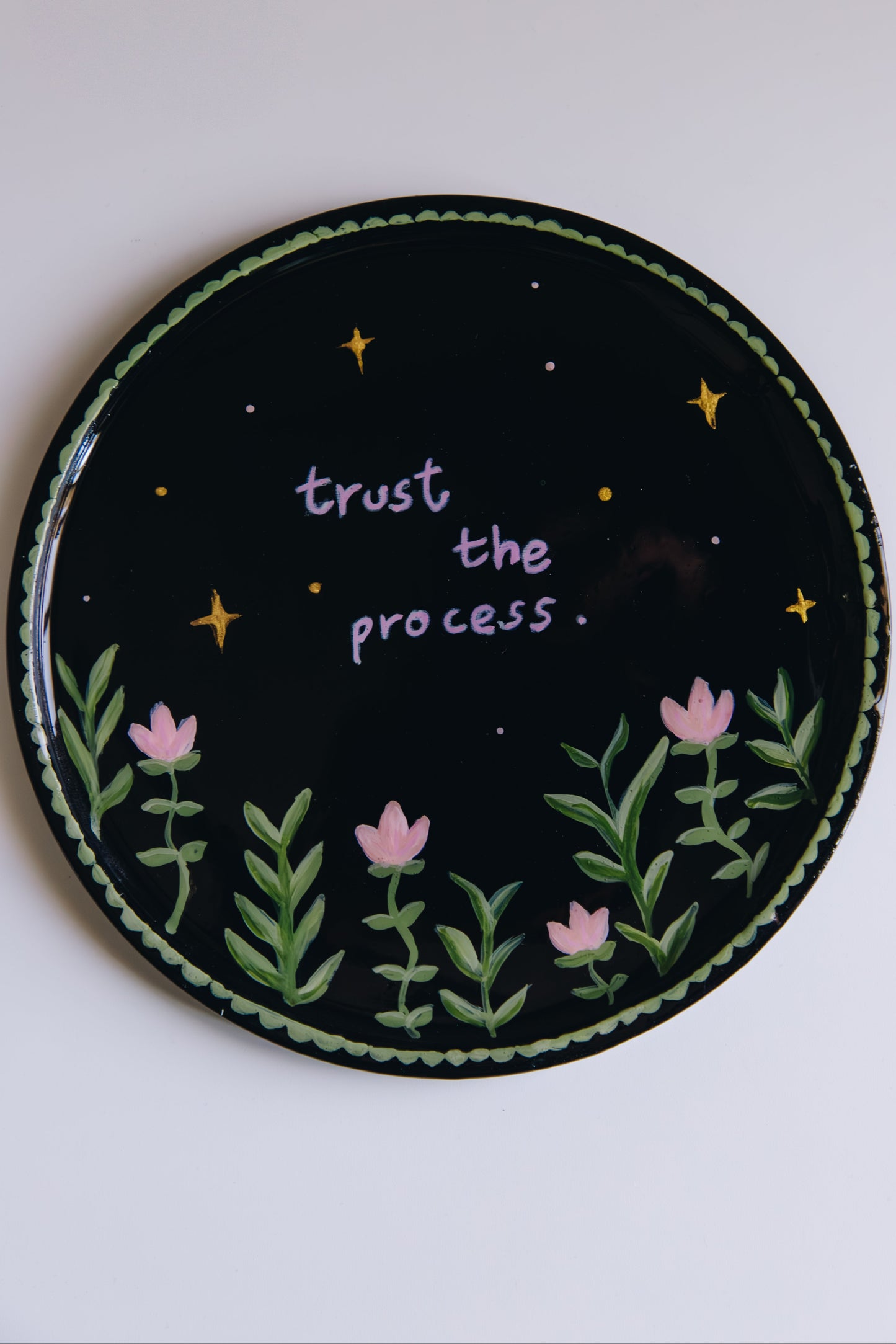 Circular dish with 'trust the process.' text, flowers, and stars on a black background.