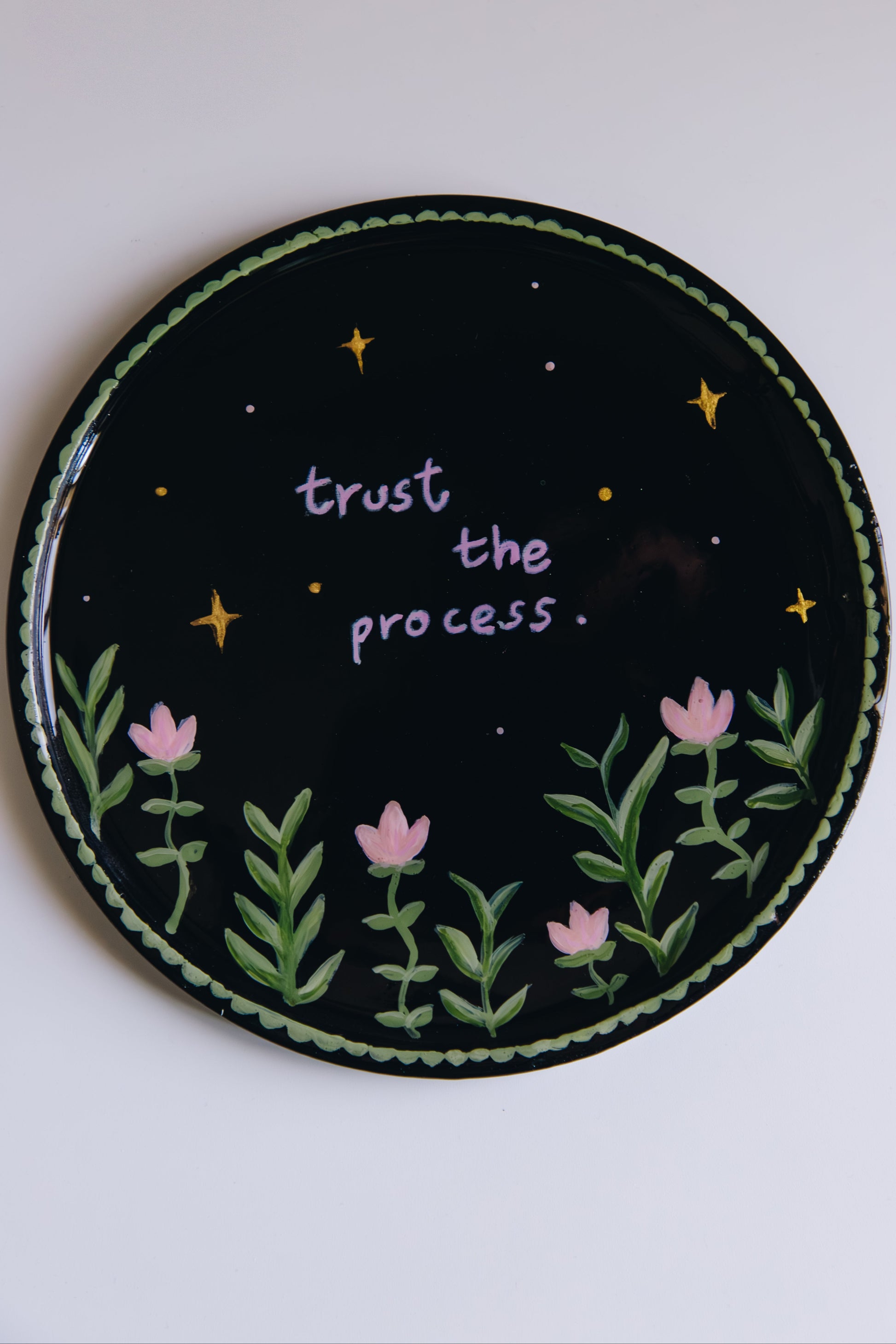 Circular dish with 'trust the process.' text, flowers, and stars on a black background.