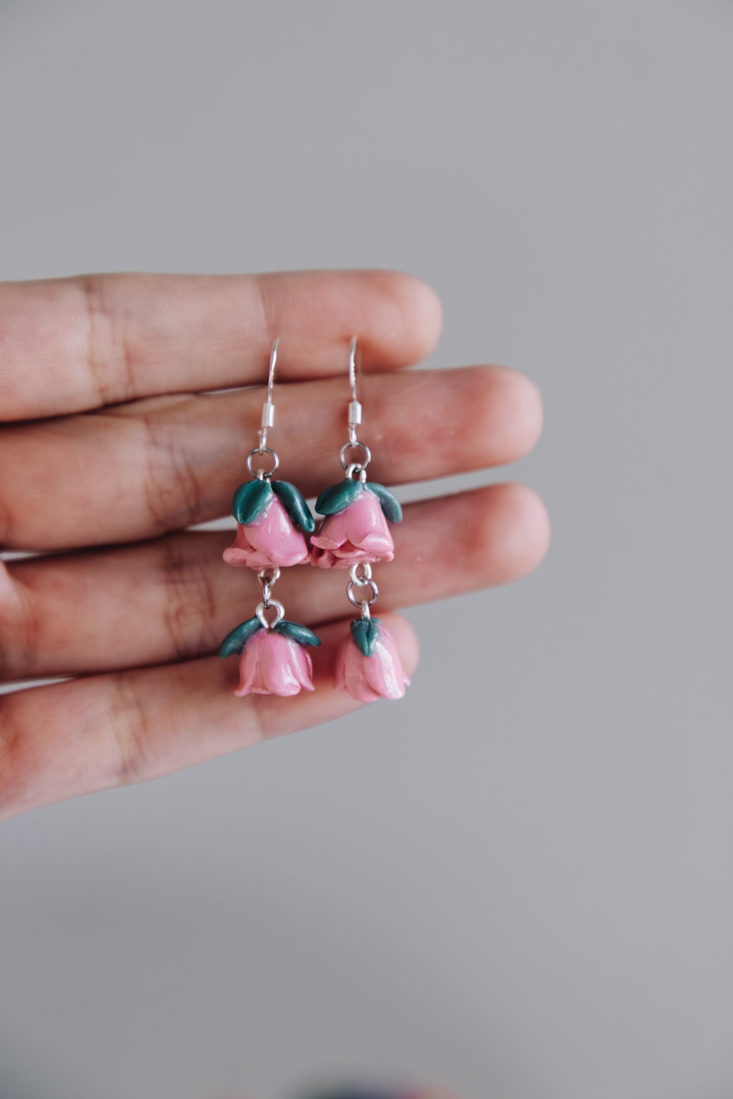 Pink floral earrings held between fingers against a gray background