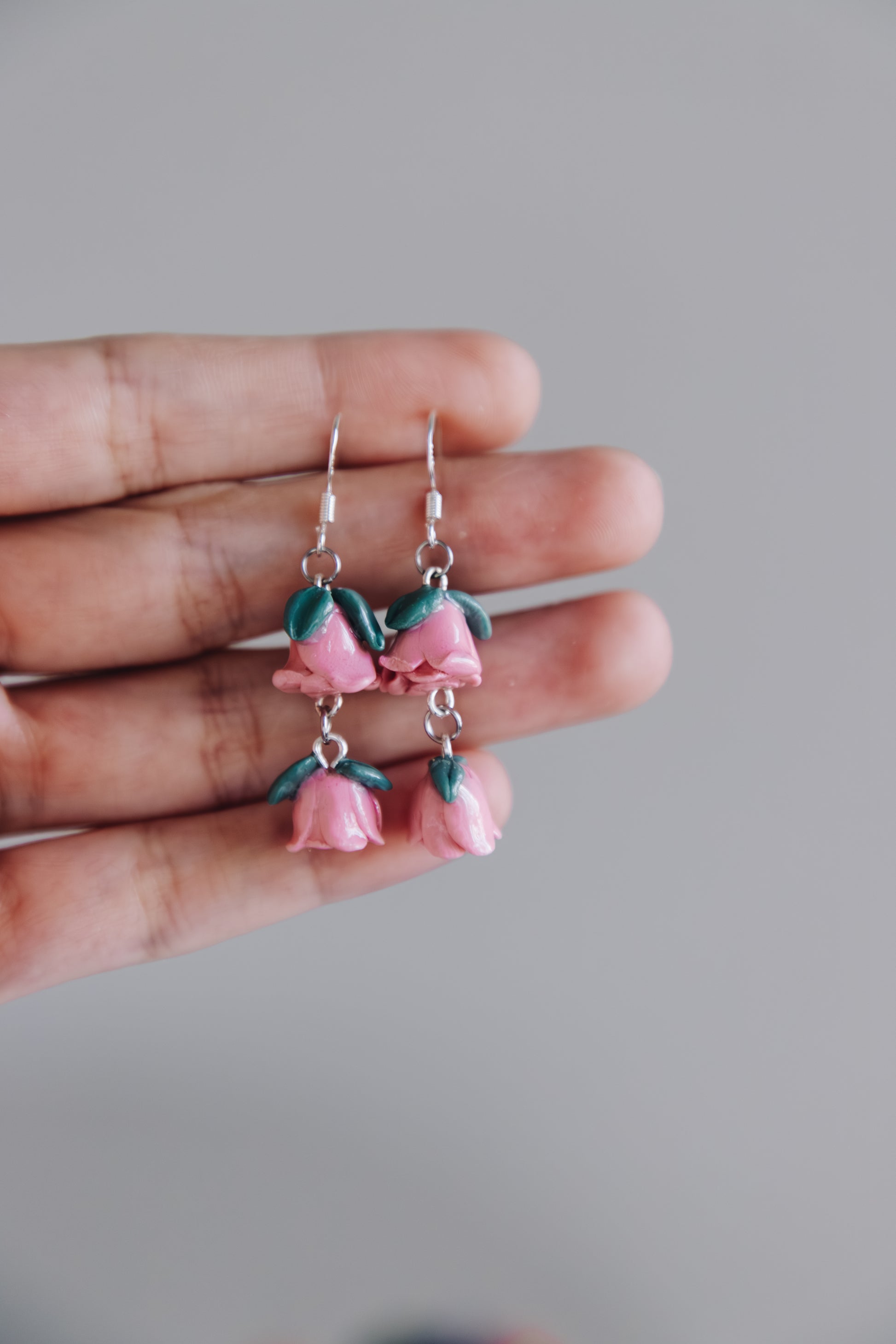 Pink floral earrings held between fingers against a gray background