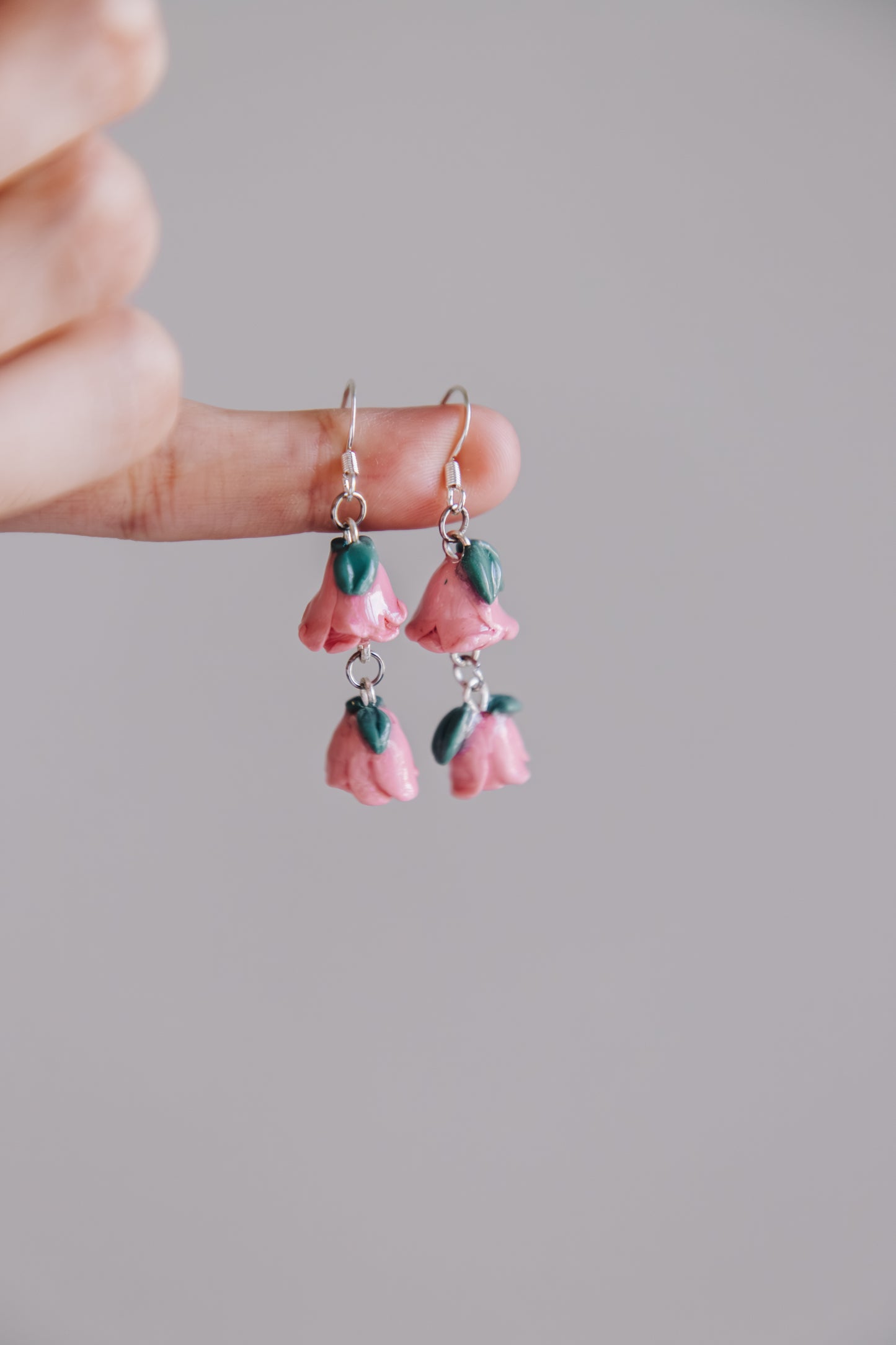 Pink flower-shaped earrings held between fingers against a neutral background
