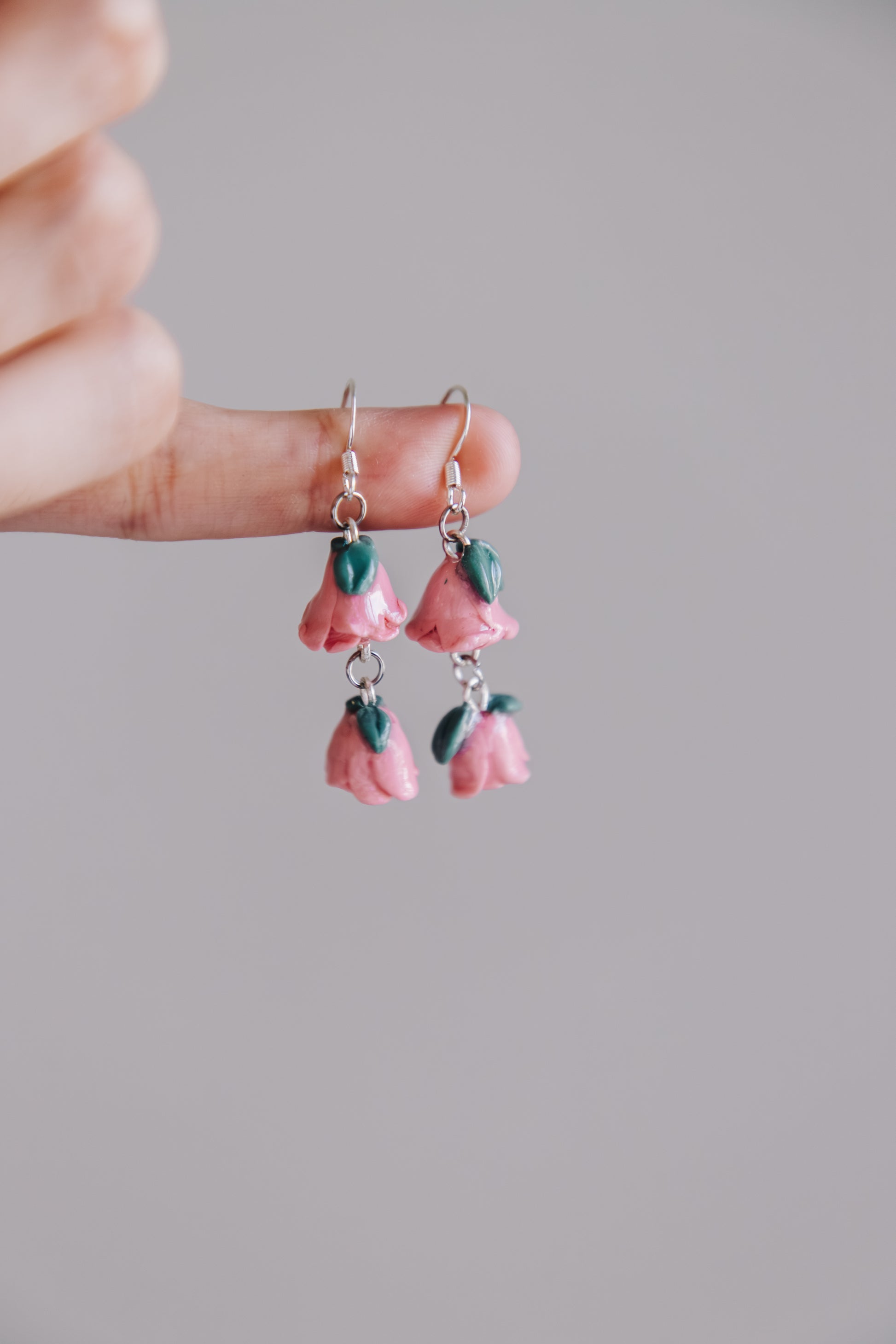 Pink flower-shaped earrings held between fingers against a neutral background