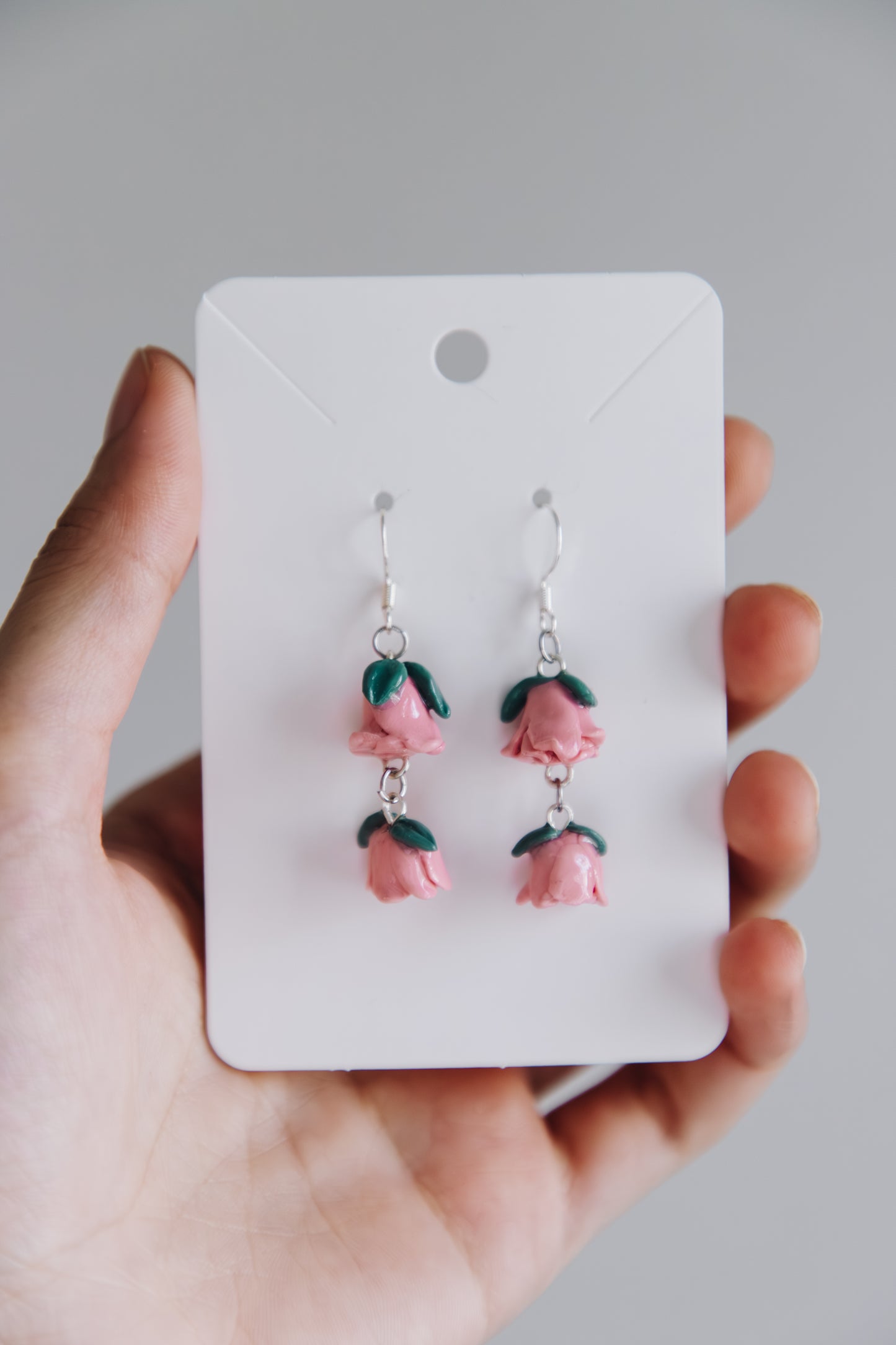 Hand holding a card with pink flower earrings on a plain background