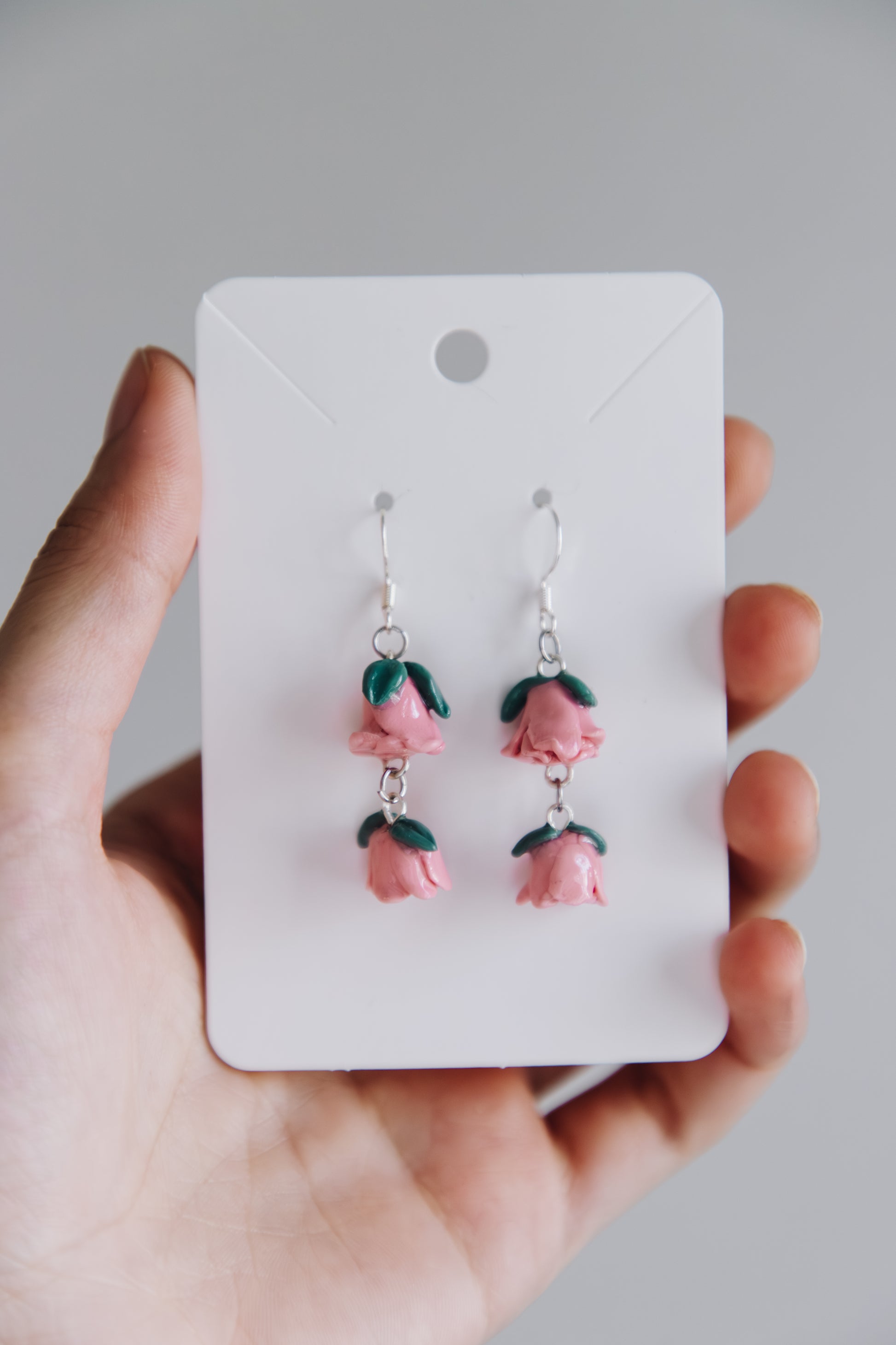 Hand holding a card with pink flower earrings on a plain background